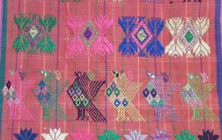 green, blue, white embroidered images on pink woven textile