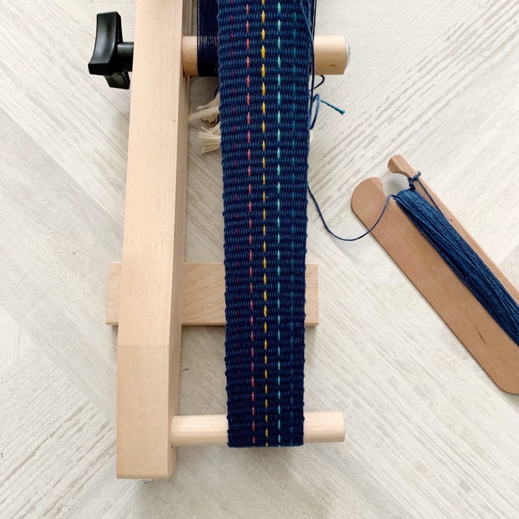a small loom and shuttle with a navy blue band being woven