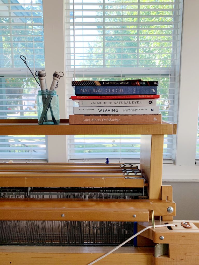 the right corner of a loom with a stack of six books on the castle, a jar with two white pirns sits next to the books